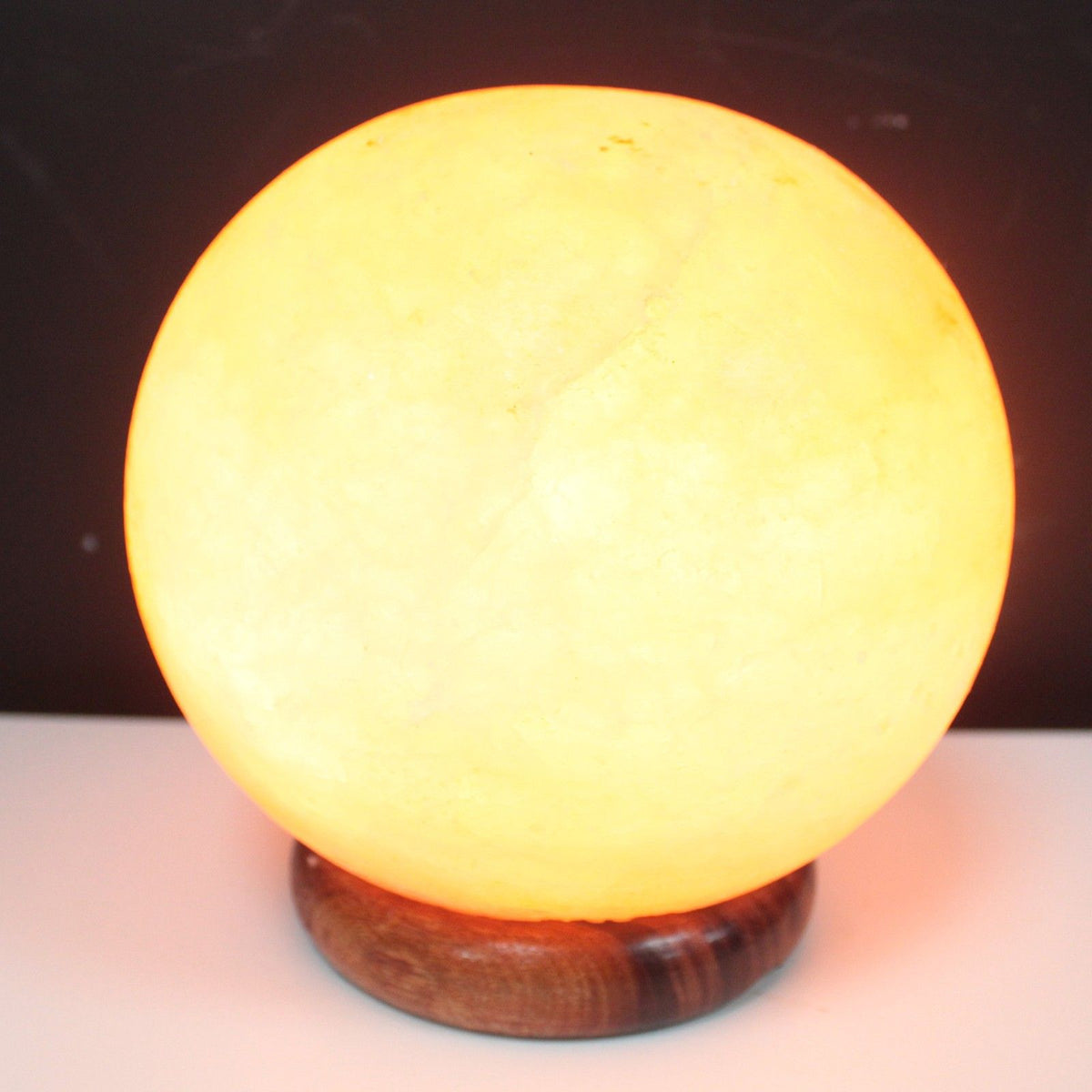 Lampe boule lumineuse en cristal de sel de l'Himalaya aux reflets orangés, posée sur un grand socle en bois. Ozora.