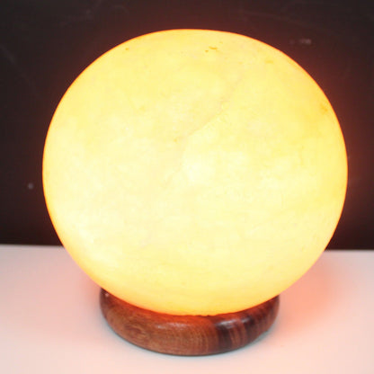 Lampe boule lumineuse en cristal de sel de l'Himalaya aux reflets orangés, posée sur un grand socle en bois. Ozora.