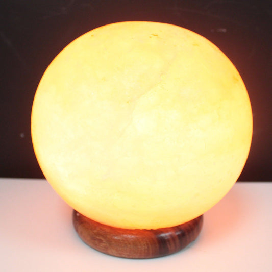 Lampe boule lumineuse en cristal de sel de l'Himalaya aux reflets orangés, posée sur un grand socle en bois. Ozora.