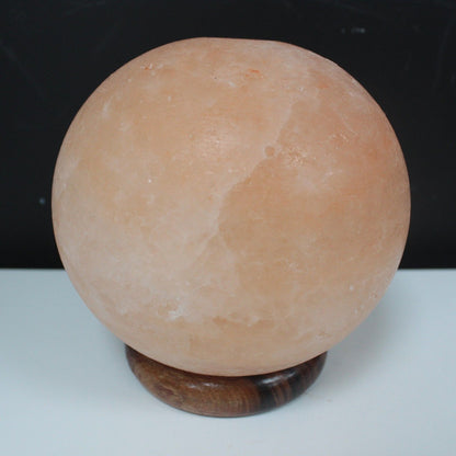 Lampe boule lumineuse en cristal de sel de l'Himalaya aux reflets orangés, posée sur un grand socle en bois. Ozora.